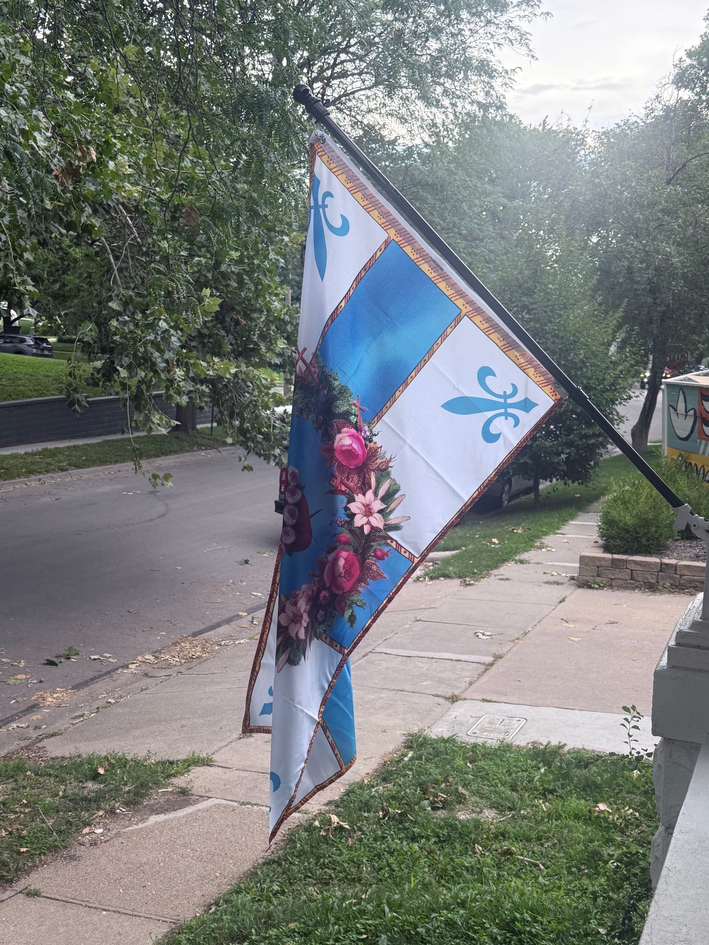 a flag with a floral design hanging on a pole on a sidewalk.