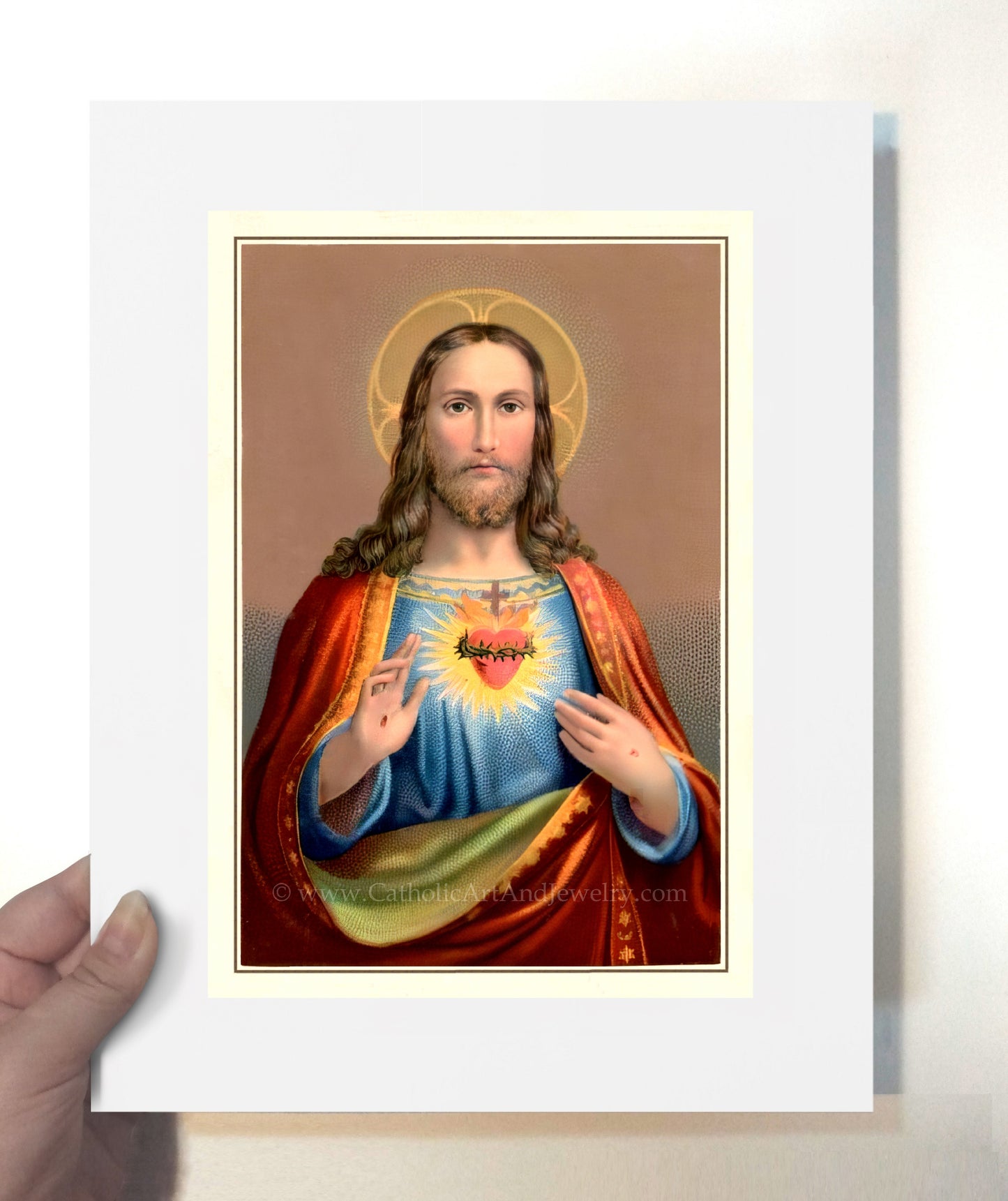 a hand holding a framed picture of jesus