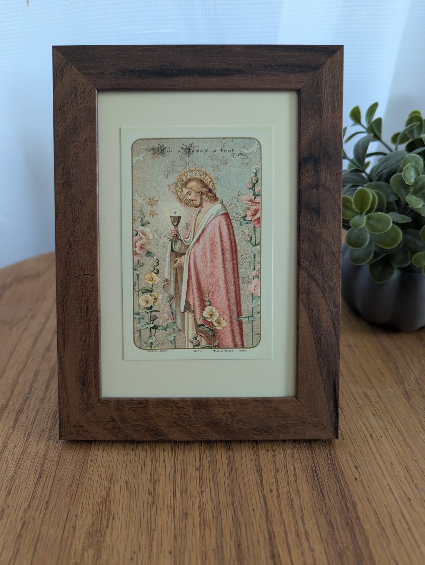 a framed religious illustration of a person in a pink robe, holding a chalice, surrounded by flowers.