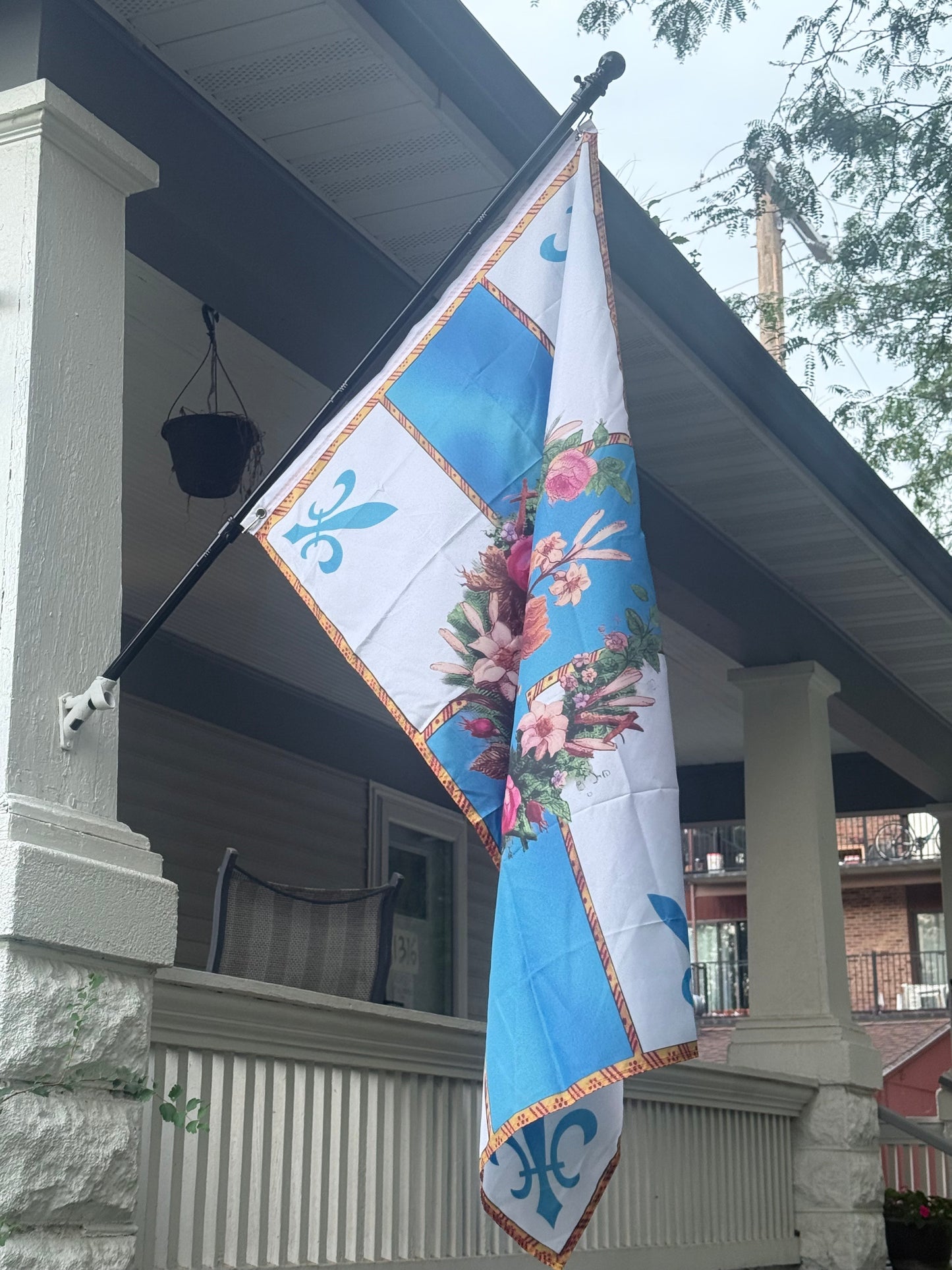 A colorful flag with a floral design is hanging from a flagpole on the side of a building.