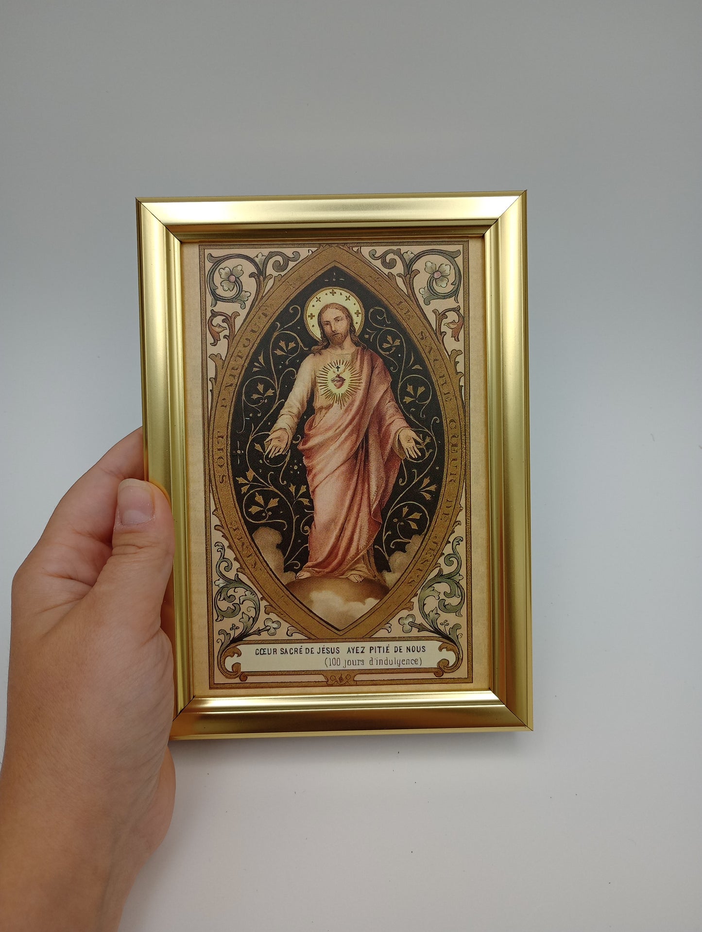 a hand holding a framed painting of a woman