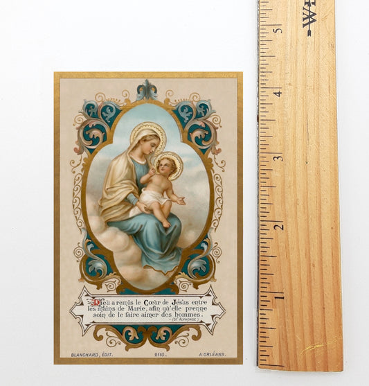 A religious card depicting the Virgin Mary holding the baby Jesus, with ornate decorations and text.