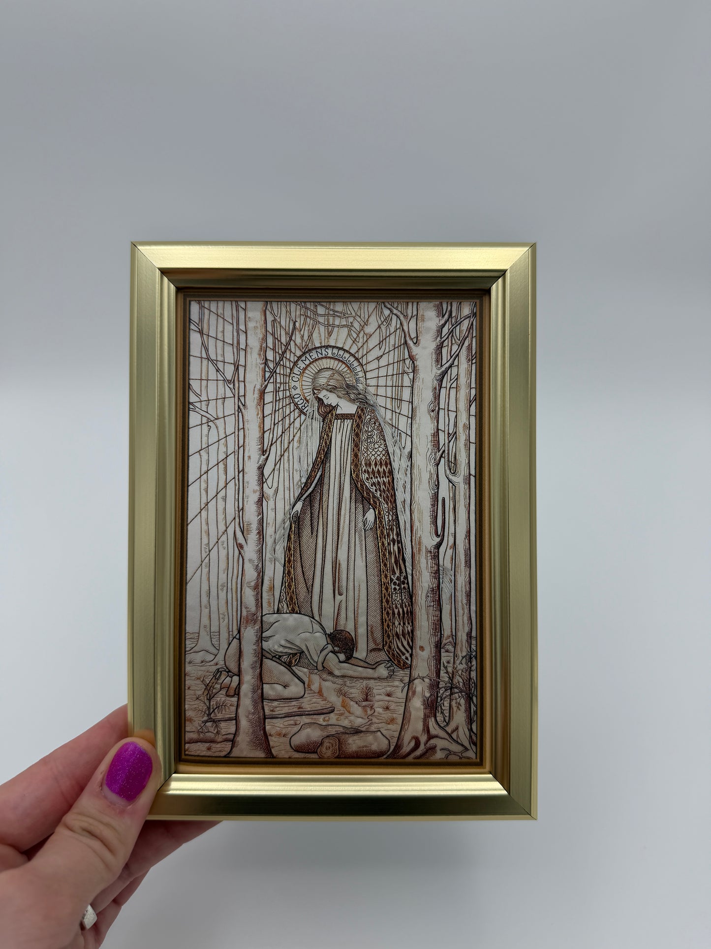 A hand is holding a framed picture of an abstract, intricate artwork with a golden frame.
