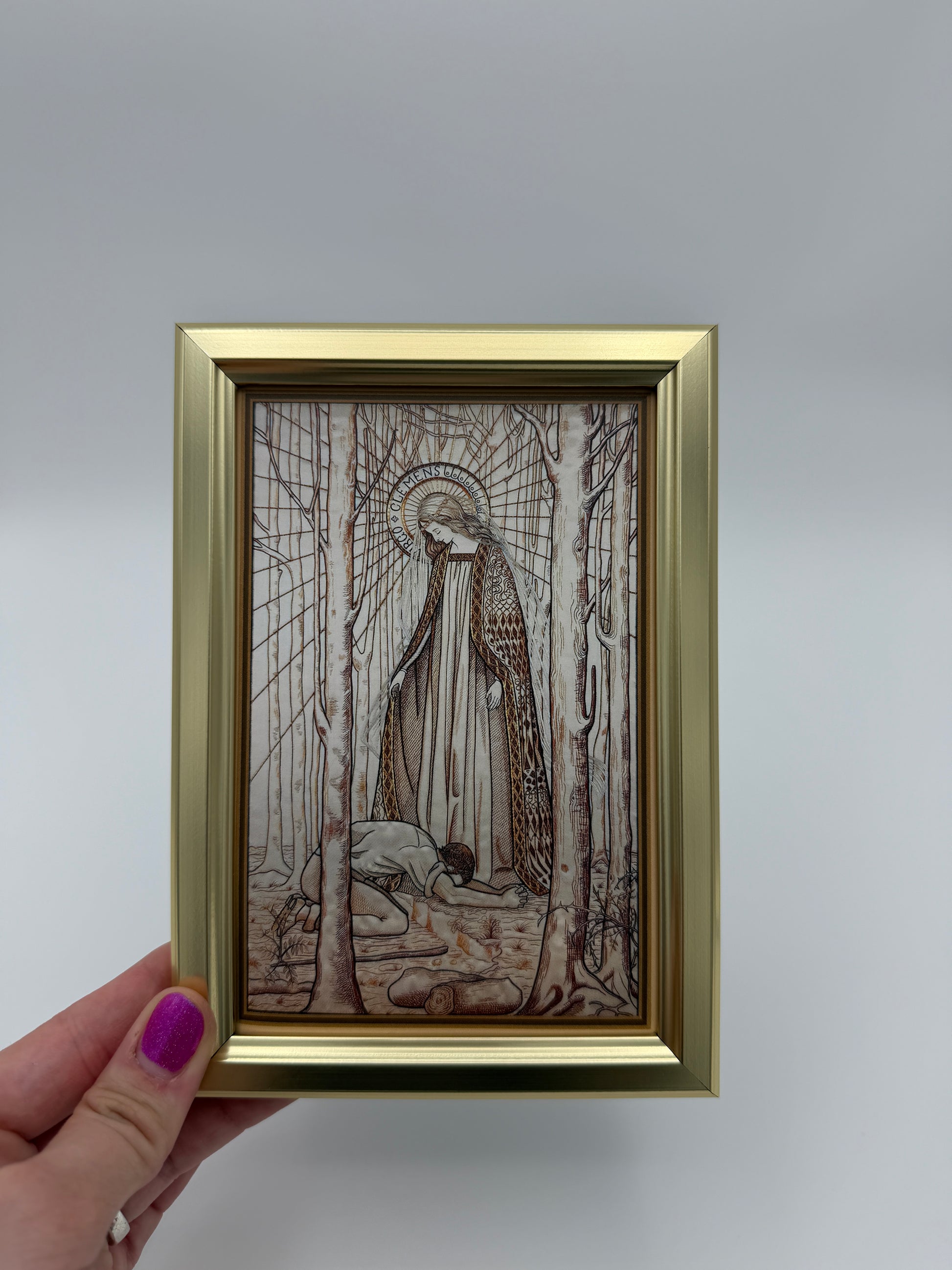 A hand is holding a framed picture of an abstract, intricate artwork with a golden frame.