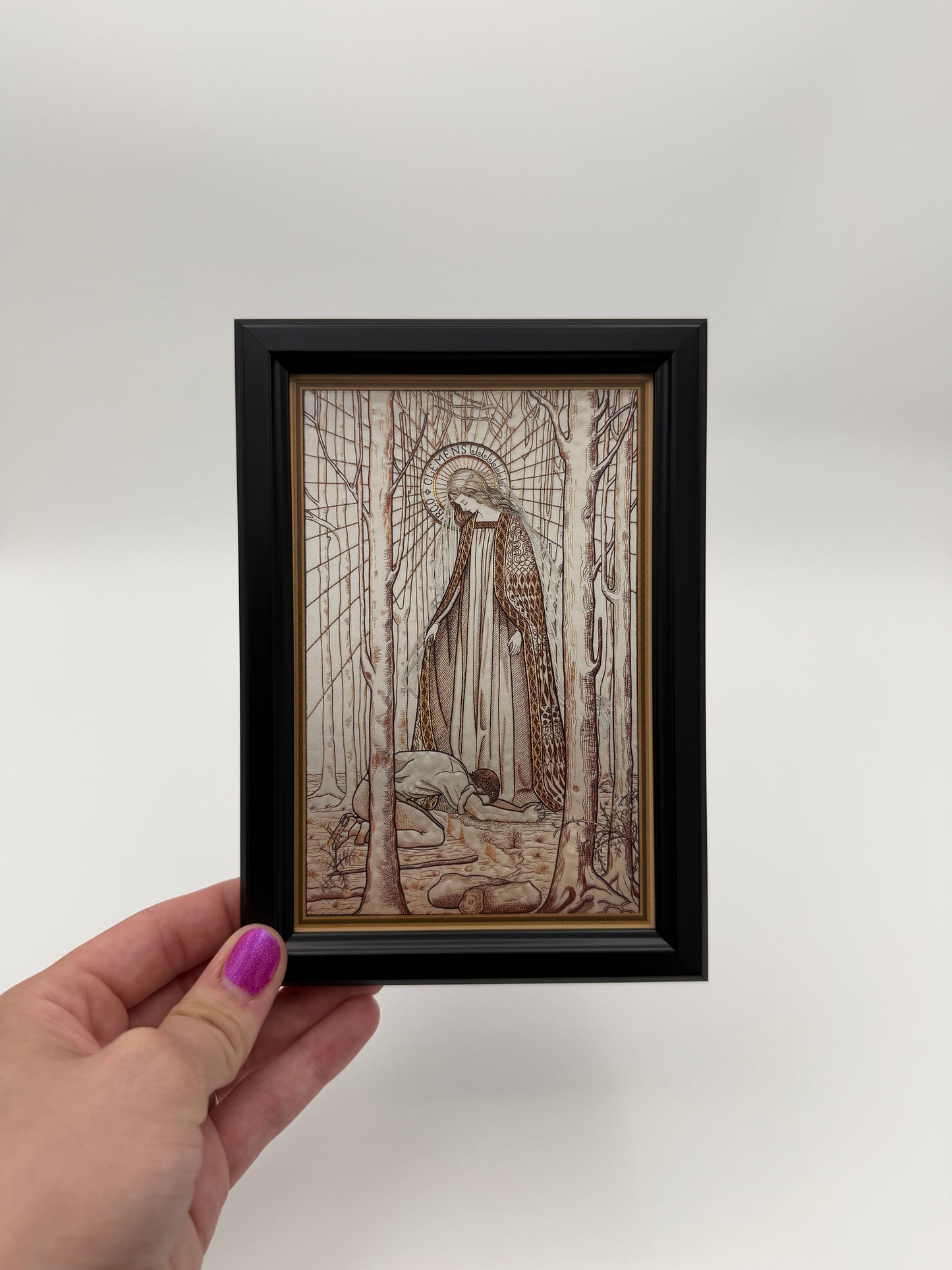 A hand is holding a framed artwork with a detailed illustration of a person sitting in a boat on a body of water.