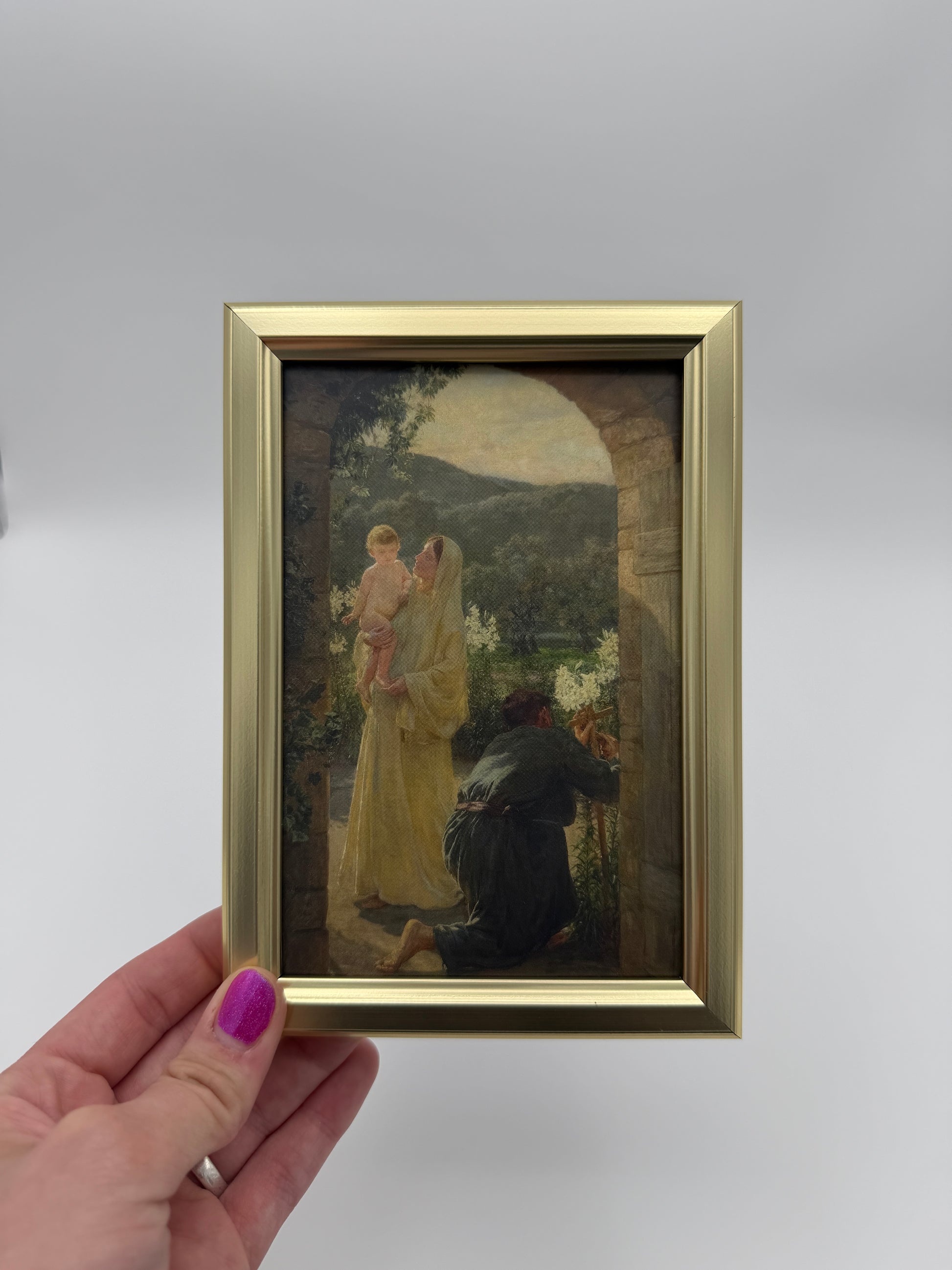 A hand holding a small framed painting of a woman in a yellow dress, with a dark background.
