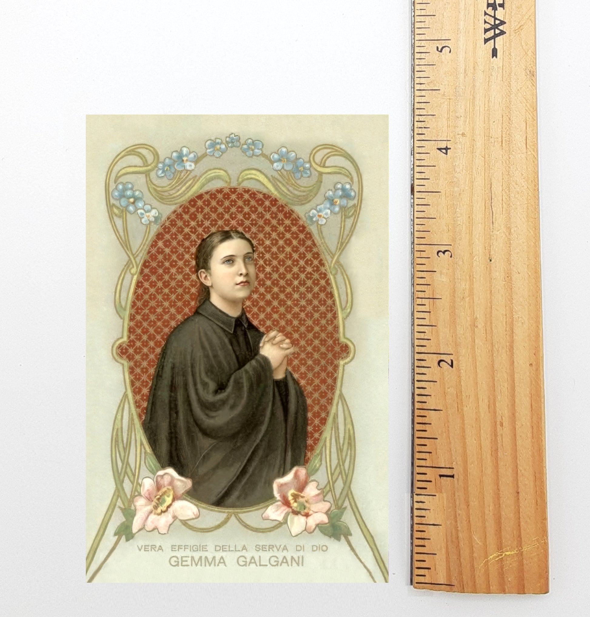 The image is a framed portrait of a person, likely a religious figure, with a floral border and a ruler for scale.