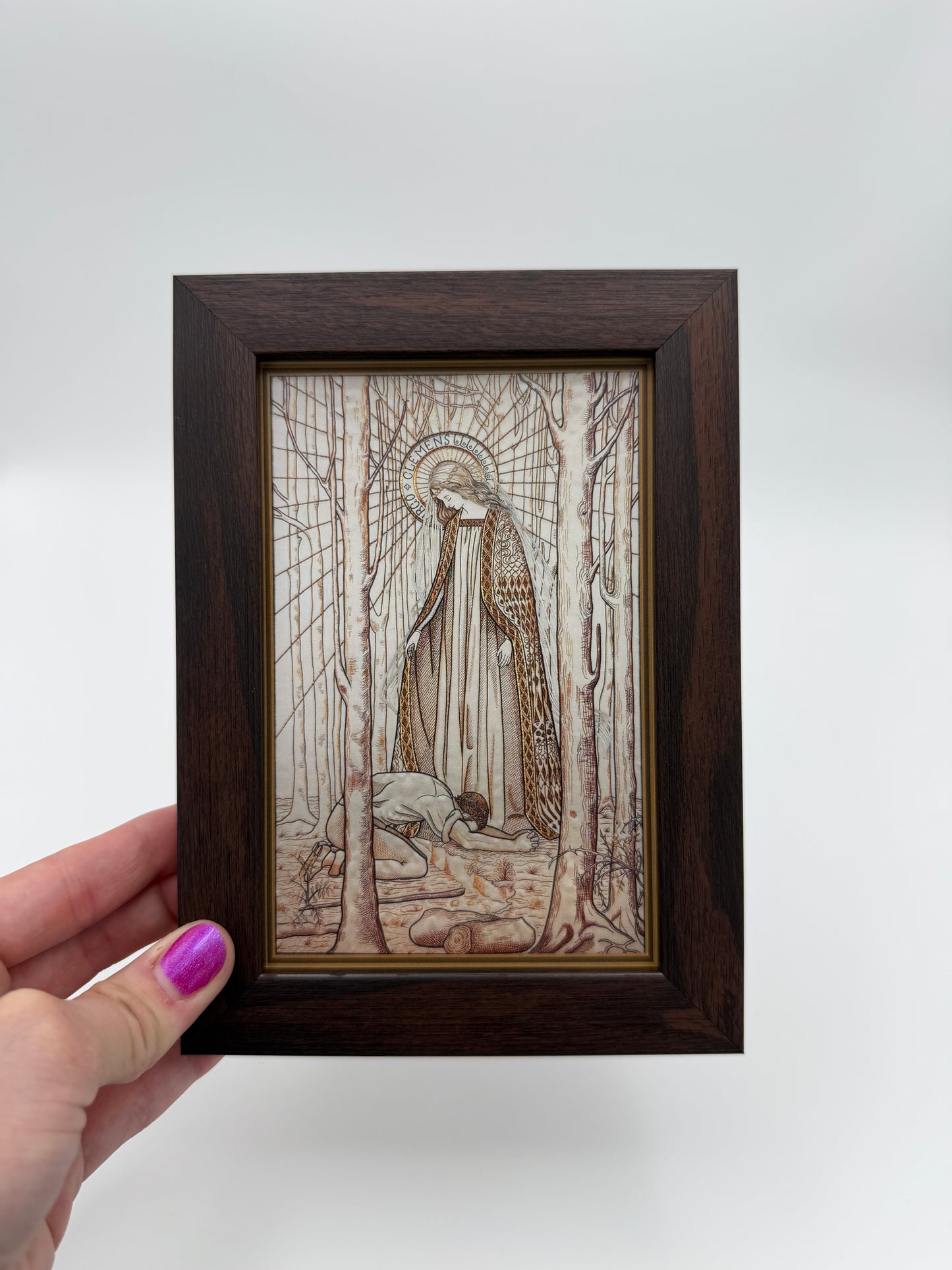 A hand is holding a framed artwork with a detailed illustration of a person in a reclining position.