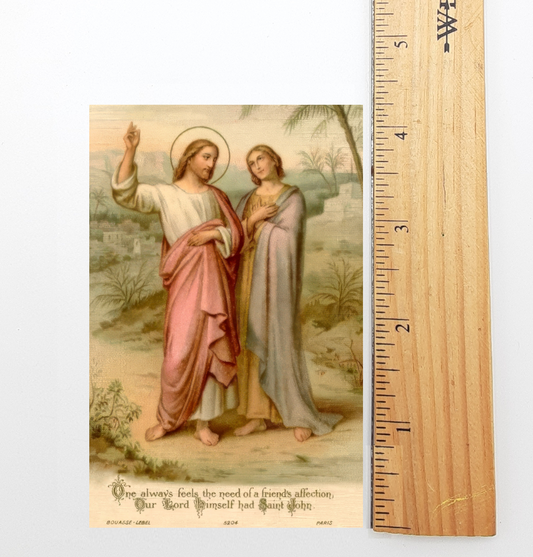 The image is a religious painting depicting two figures, likely Jesus and Mary, standing in a natural setting. The painting is framed by a wooden ruler, which is marked with measurements in inches. The text below the painting reads "One always feels the need of a friendly affection. Our Lord Himself had said, 'Be kind to one another.' BOUQUET-LEBEL, PARIS, 624."