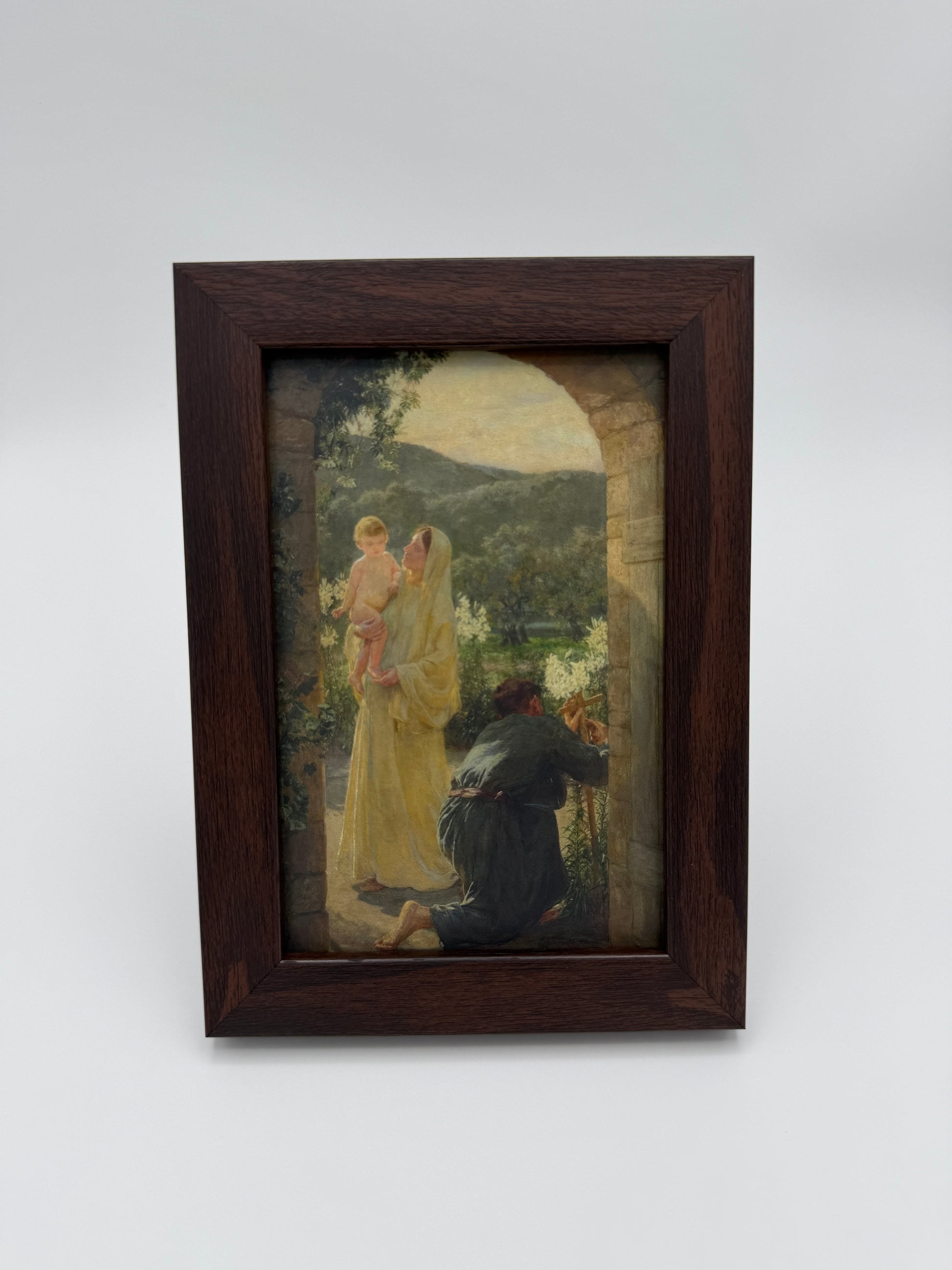 The image is a framed painting depicting a woman in a yellow dress and a child in a white dress, standing in a garden setting with trees and a building in the background.