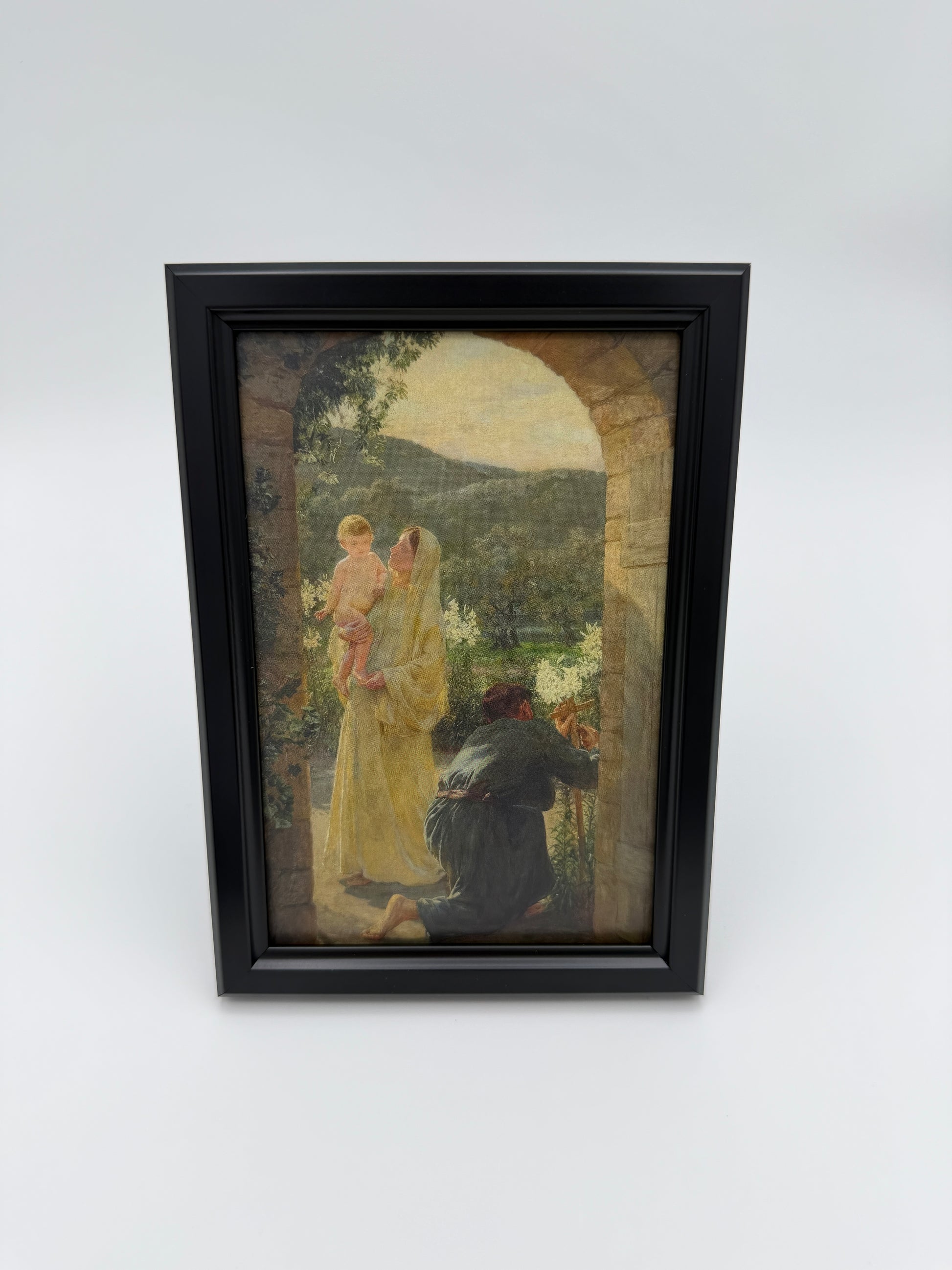 The image is a framed painting depicting a woman in a yellow dress and a child in a white dress, standing in a garden setting with trees and a stone archway in the background.