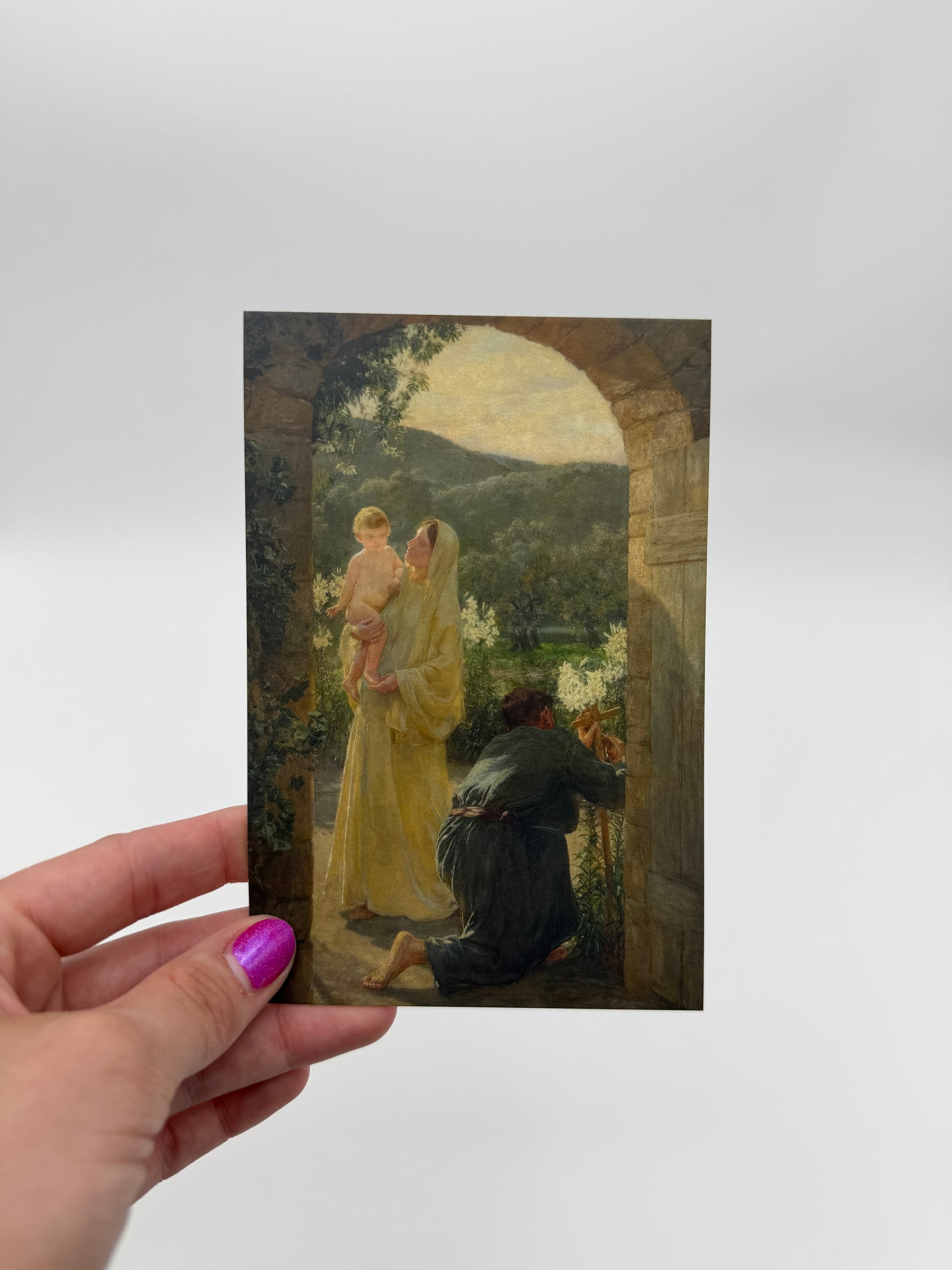 A hand holding a framed painting of a woman in a yellow dress, with a man in a black suit standing next to her.