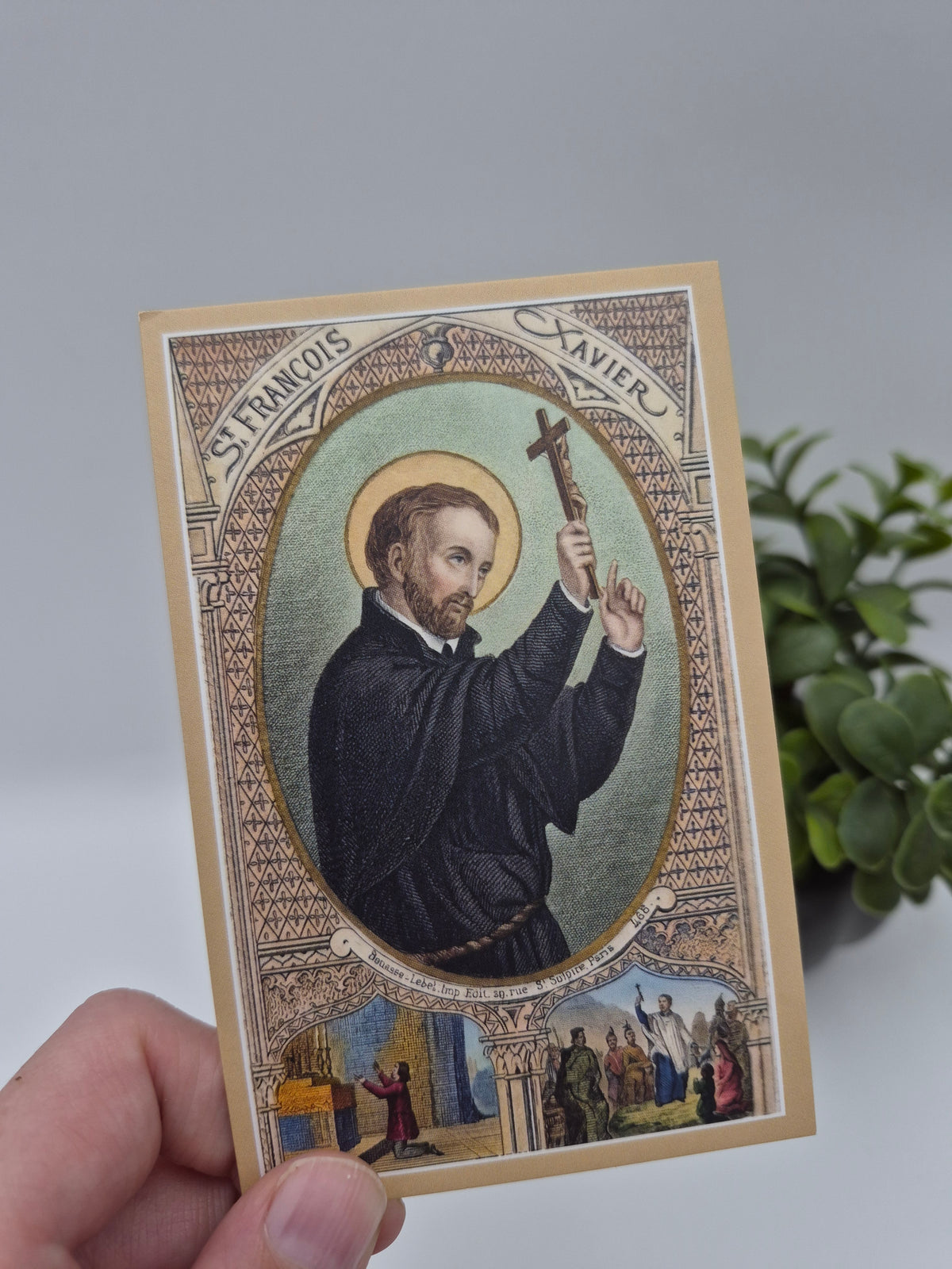 A hand holding a card with an illustration of a person wearing a black robe and holding a cross.