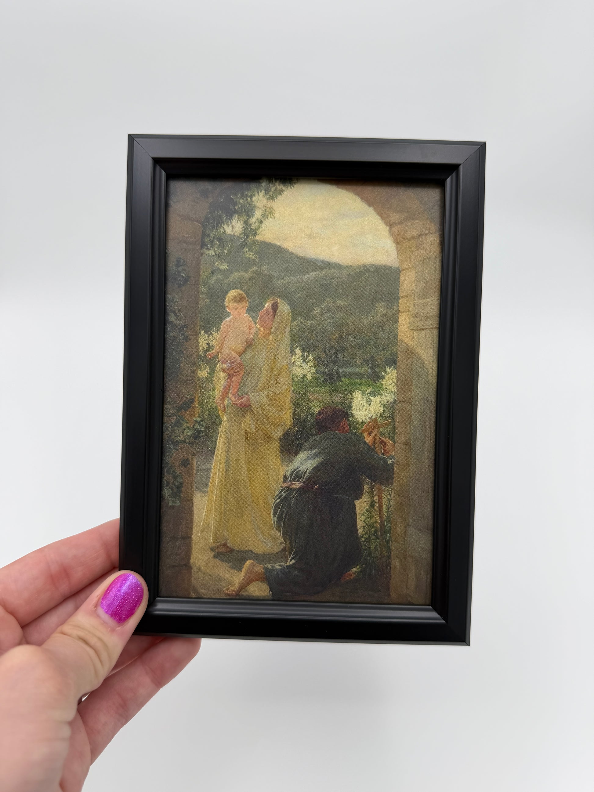 A framed painting of a woman and child is being held up against a white background.