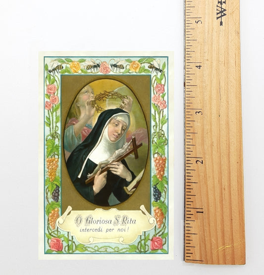 The image is a religious card featuring a depiction of a nun, with a cross and grapes in the background. The card is framed by a decorative border with floral elements. The card is approximately 6 inches tall, as indicated by the ruler placed next to it.
