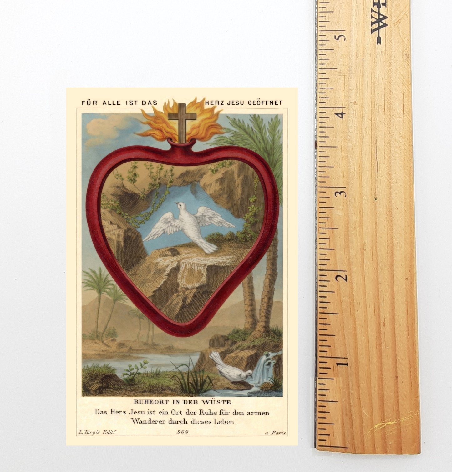 The image is a vintage religious card featuring a heart-shaped illustration with a cross at the top, surrounded by a landscape with palm trees and a river. The card is approximately 5 inches tall, as indicated by the ruler next to it.